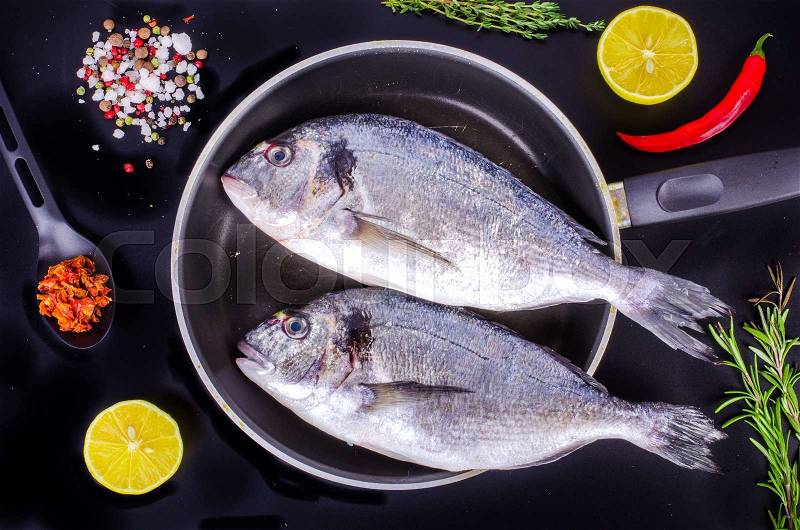 Fresh raw gilthead fishes with lemon, herbs, salt on black background. Healthy food concept. Food frame, stock photo