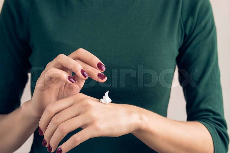 Woman in a green T-shirt and a maroon manicure applying hand cream, stock photo