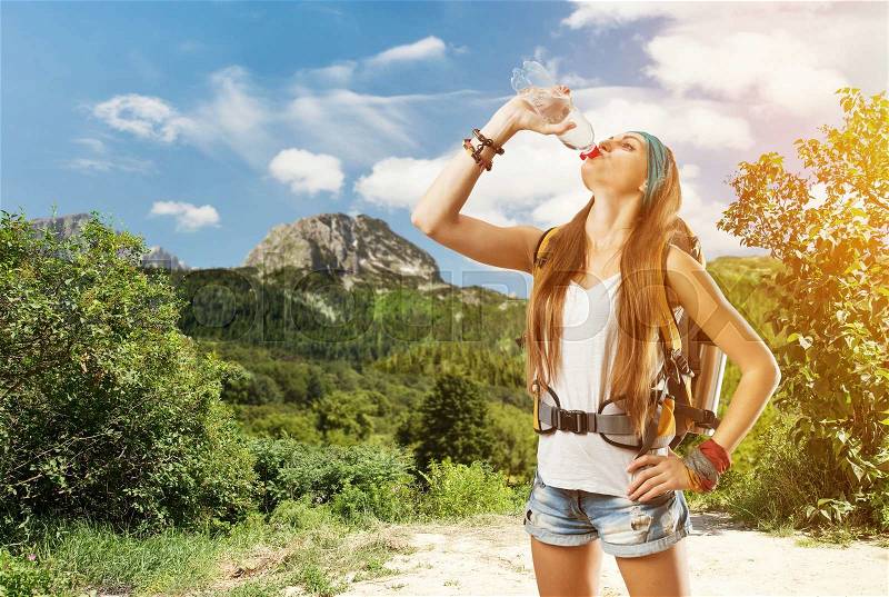 Hiking girl with backpack in the forest is drinking water, stock photo