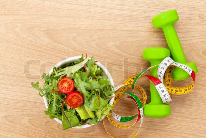 Dumbells, tape measure and healthy food over wooden table. Fitness and health, stock photo