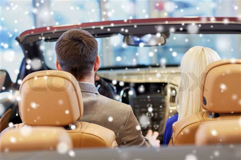 Auto business, car sale, consumerism and people concept - close up of couple sitting in cabrio car at auto show or salon over snow effect from back, stock photo