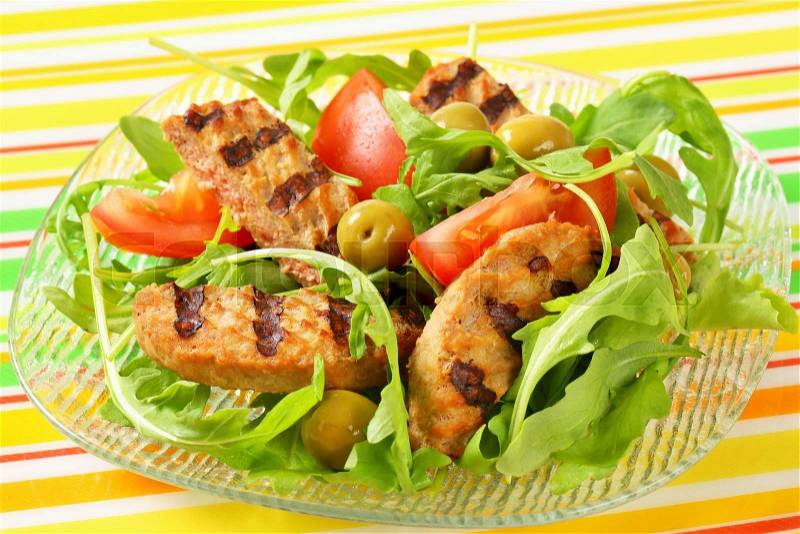 Sliced grilled patty on nest of rocket salad with tomato and olives, stock photo