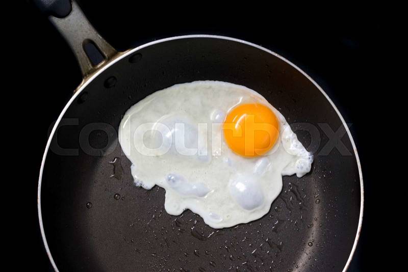 Fried egg in frying pay, top view on black background, stock photo