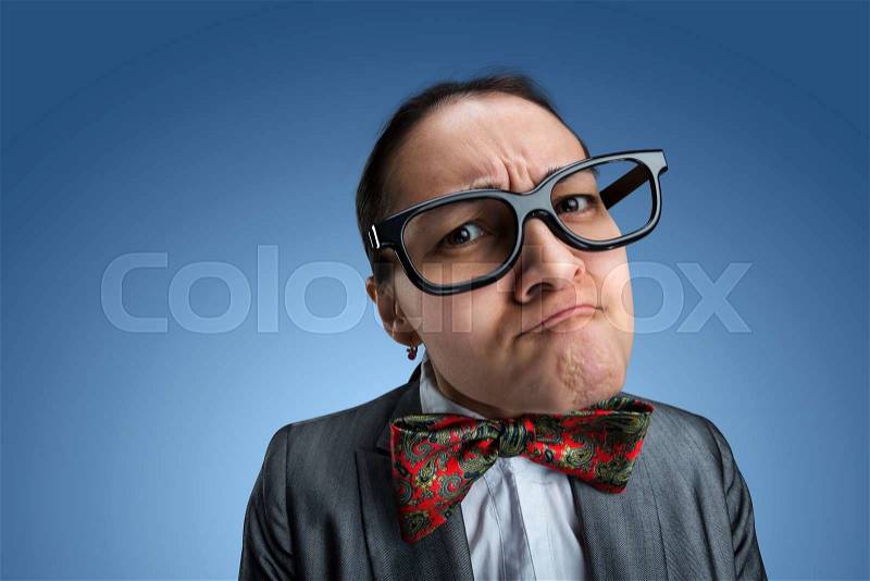 Funny nerd girl in glasses looks at you over blue background, stock photo