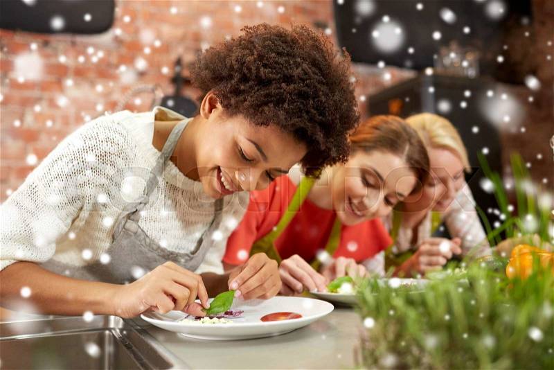 Cooking class, friendship, food and people concept - happy women cooking and decorating plates with dishes in kitchen over snow effect, stock photo