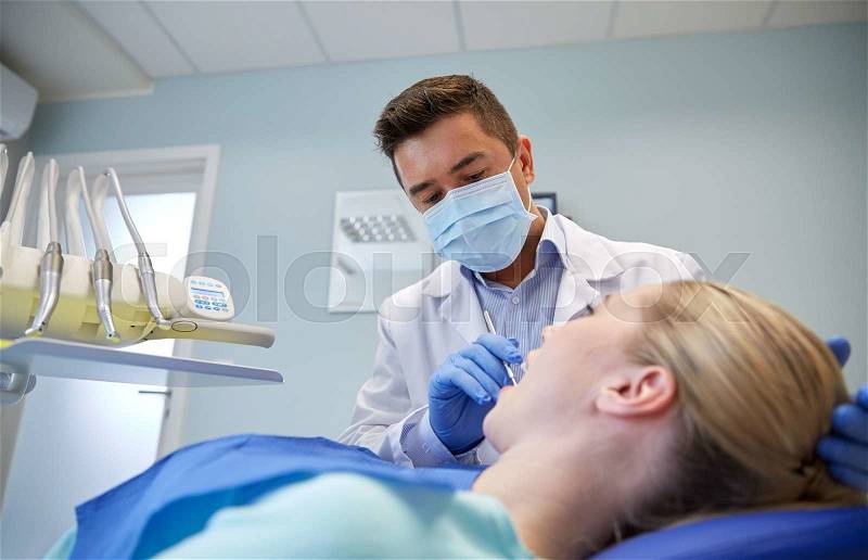 People, medicine, stomatology and health care concept - male dentist in mask checking female patient teeth up at dental clinic office, stock photo