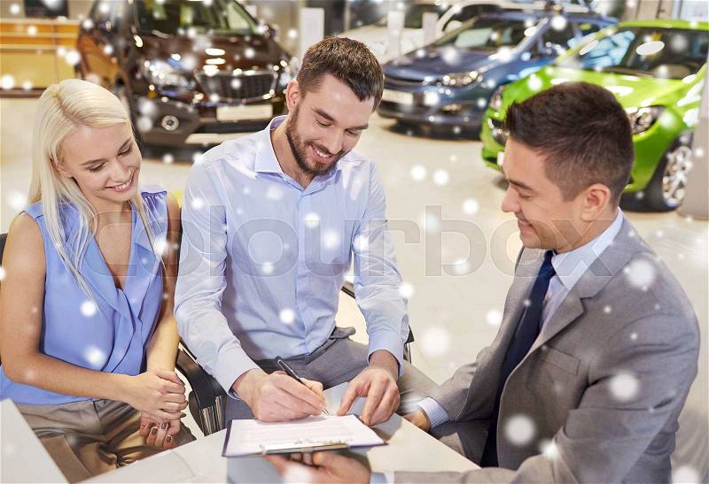 Auto business, sale and people concept - happy couple with dealer buying car and signing documents in auto show or salon over snow effect, stock photo