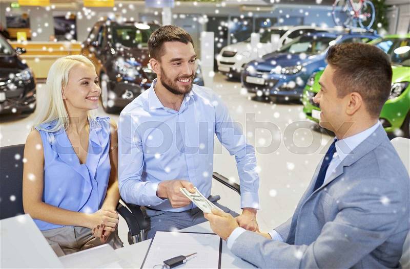 Auto business, sale and people concept - happy couple with money buying car from dealer in auto show or salon over snow effect, stock photo