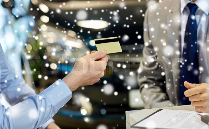 Auto business, sale and people concept - close up of customer giving credit card to car dealer in auto show or salon over snow effect, stock photo