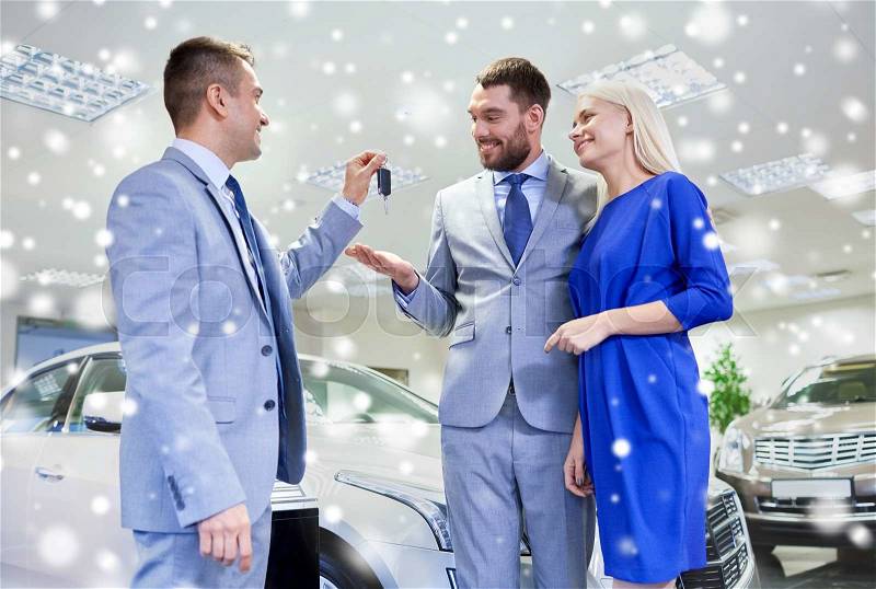 Auto business, sale and people concept - happy couple with dealer giving car key in auto show or salon over snow effect, stock photo