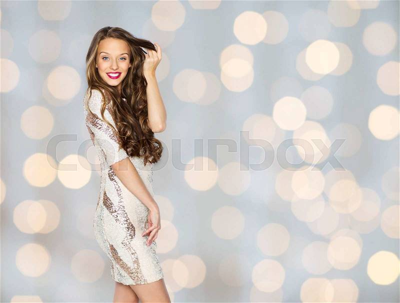 People, style, holidays, hairstyle and fashion concept - happy young woman or teen girl in fancy dress with sequins touching long wavy hair over lights background, stock photo