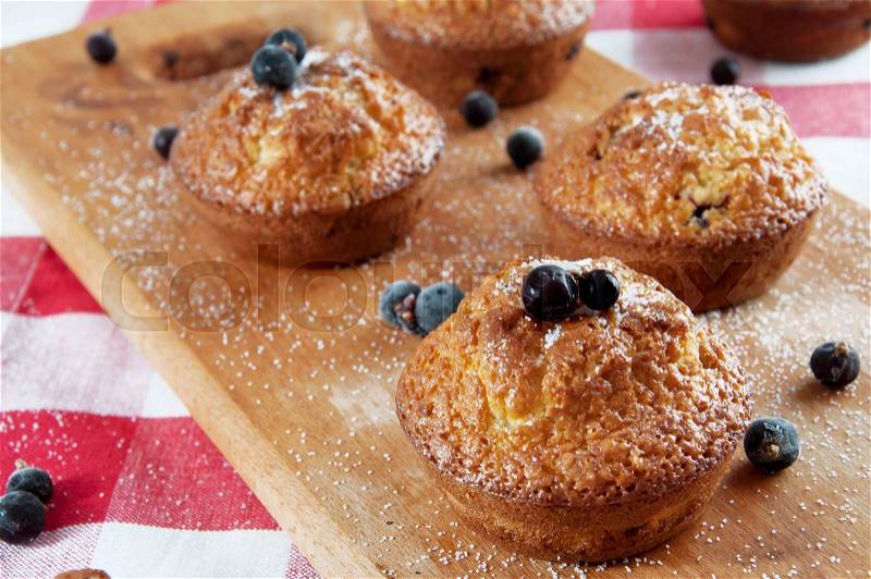 Freshly baked muffins sprinkles with sugar and black currant berries on wooden plate, stock photo