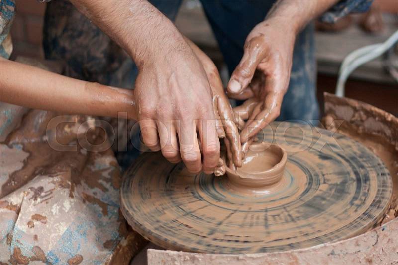 Potter teaches to sculpt in clay pot on the turning pottery wheel, stock photo