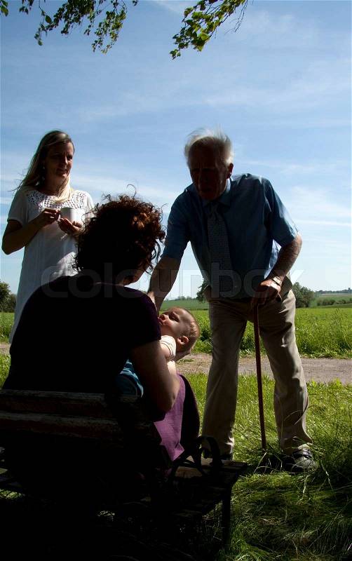 Old man with walking stick greeting a baby and mother, stock photo