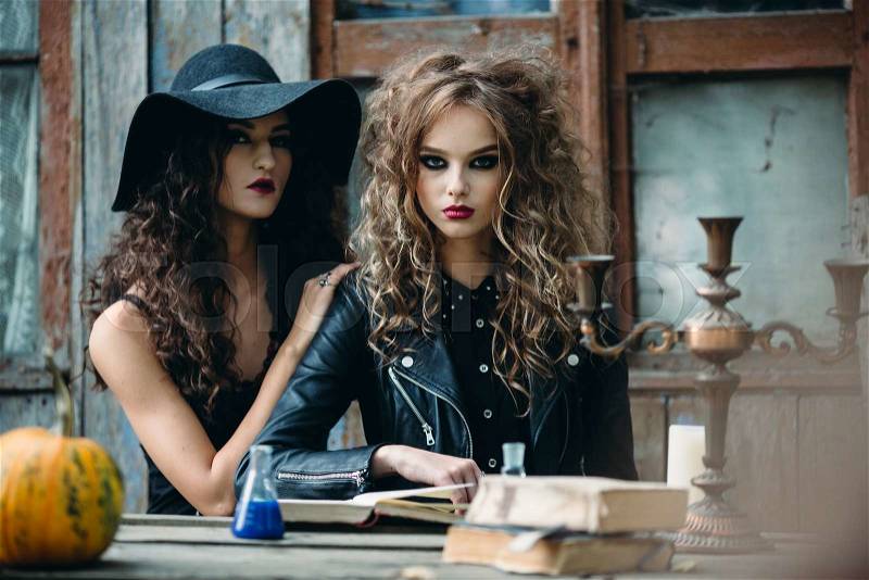Two vintage witch sitting at the table in an abandoned place on the eve of Halloween, stock photo