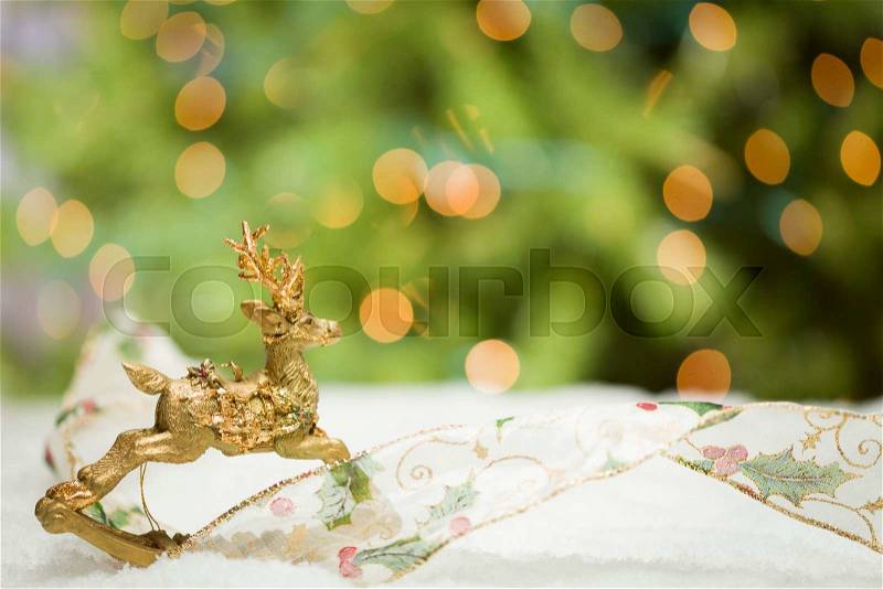 Decorative Christmas Reindeer Ornament and Ribbon on Snow with Tree and Lights Background, stock photo