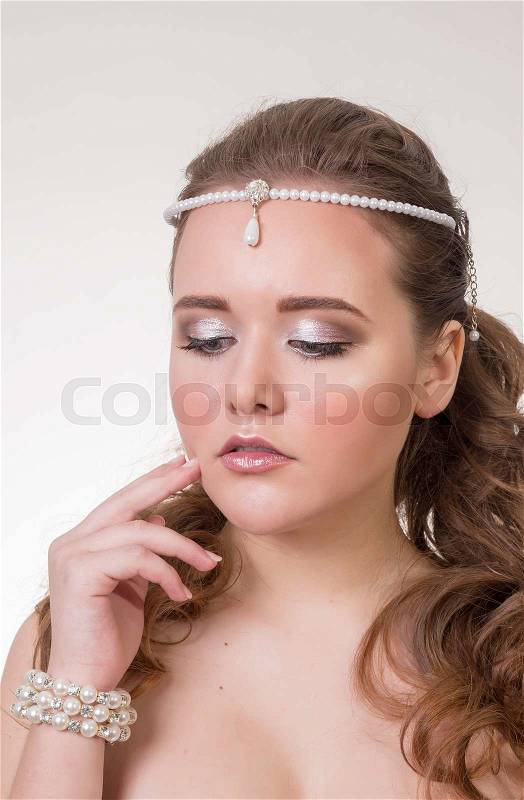 Young brunette lady with beautiful hair and ornaments on a gray background, stock photo