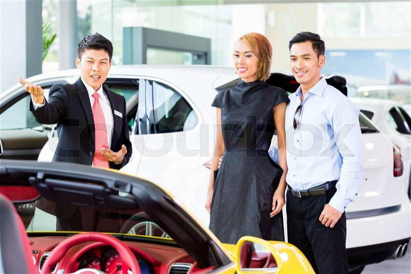 Asian couple buying car in auto dealership consulting the salesman , stock photo