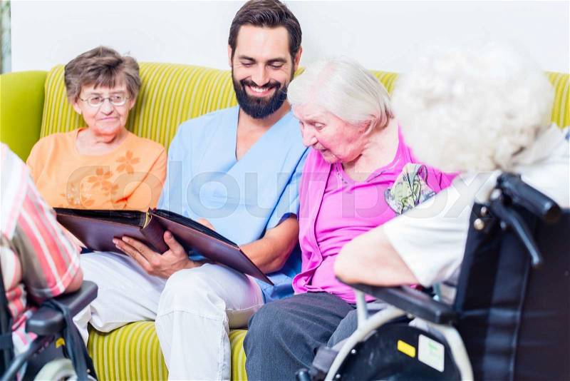 Geriatric nurse looking at pictures with seniors in nursery home, stock photo
