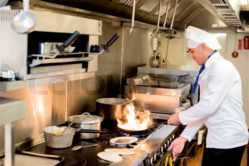Chef preparing cuisine in hotel kitchen, stock photo