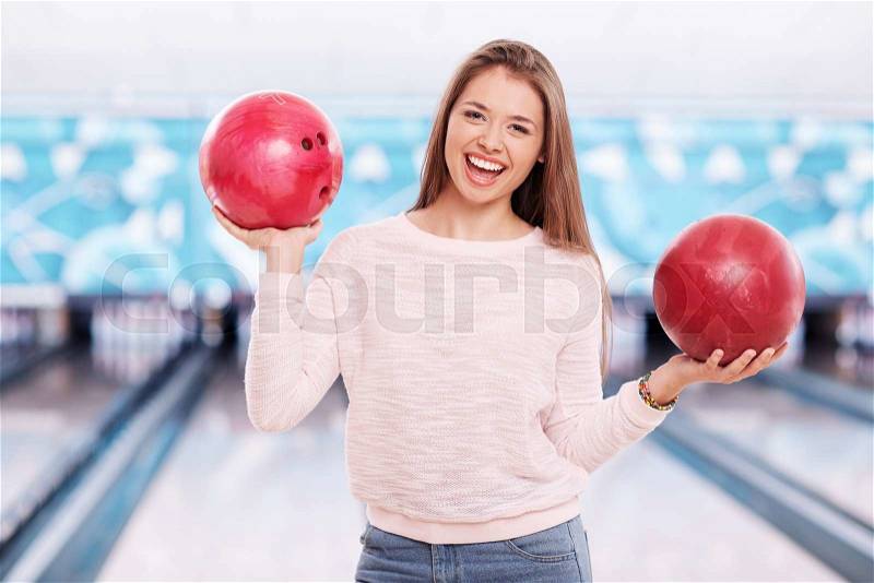 Happy girl with bowling balls looking at camera, stock photo
