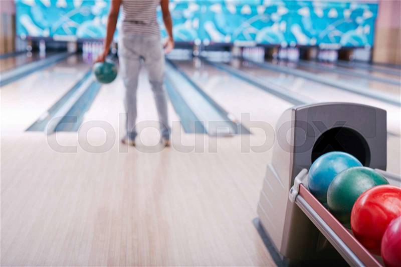 Multi-color bowling balls on background of guy standing in alley, stock photo