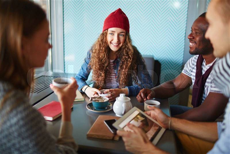 Young female in knitted cap and her friends spending time in cafe, stock photo