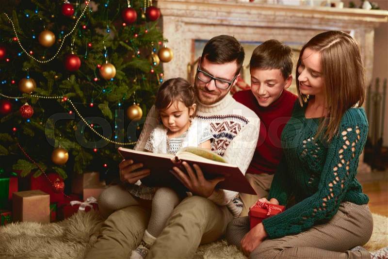 Happy family of four reading together on Christmas evening, stock photo