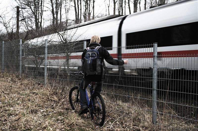 A man looking at a train driving by while on his push bike, stock photo