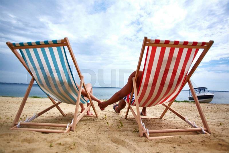 Couple holding hands and sunbathing on the beach, stock photo