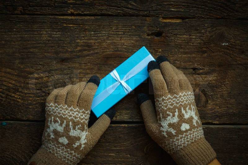 Hands in winter gloves with christmas gift box on wooden background, stock photo