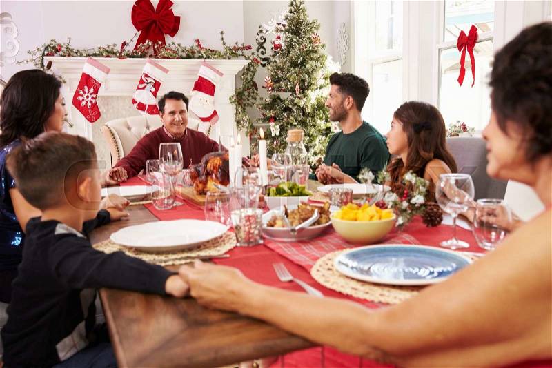 Family With Grandparents Saying Grace Before Christmas Meal, stock photo