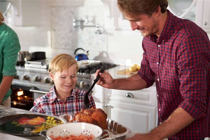 Father And Son Cooking Roast Turkey In Kitchen Together, stock photo