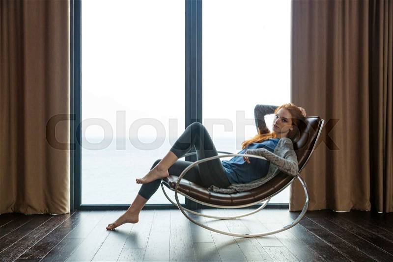 Portrait of a beautiful redhead woman sitting on rocking chair at home, stock photo