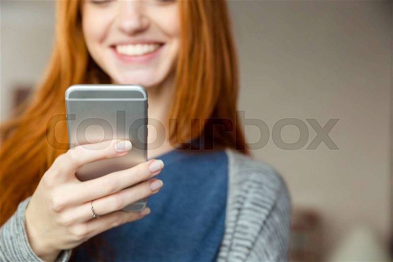Cropped image of a smiling redhead woman using smartphone, stock photo