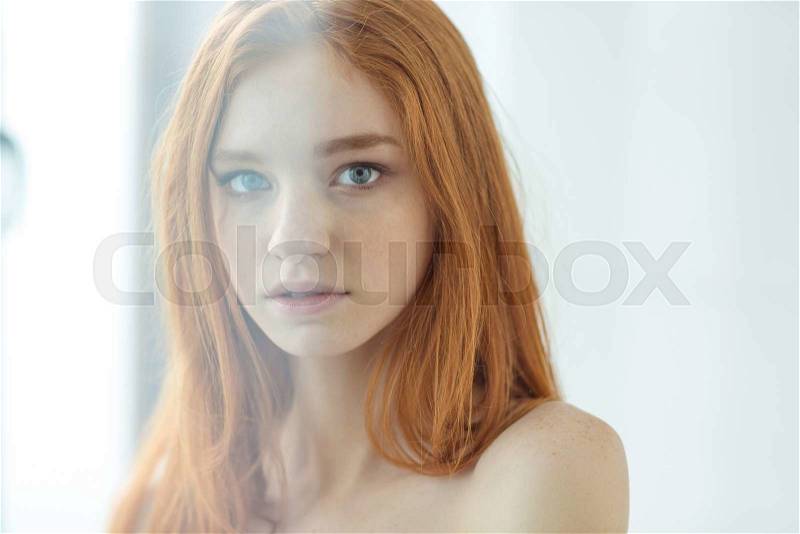 Portrait of a charming redhead woman looking at camera through the window , stock photo