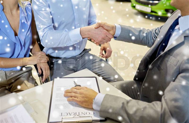 Auto business, car sale, gesture and people concept - close up of customers couple with dealer shaking hands in auto show or salon over snow effect, stock photo