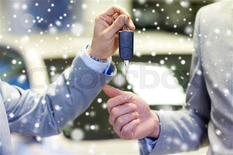 Auto business, car sale, deal and people concept - close up of male hands with car key in auto show or salon over snow effect, stock photo