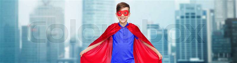 Carnival, childhood, power and people concept - happy boy in red super hero cape and mask over city buildings background, stock photo