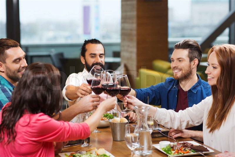 Leisure, celebration, food and drinks, people and holidays concept - smiling friends having dinner and drinking red wine at restaurant, stock photo