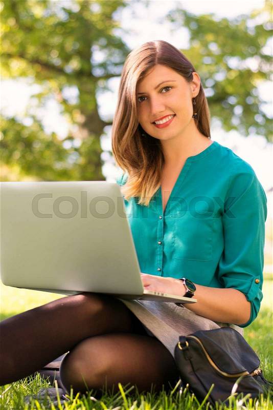 Dark haired woman with slight freckles complexion; working with her laptop in a park. Could be a business woman in her break or a free spirit entrepreneur, stock photo