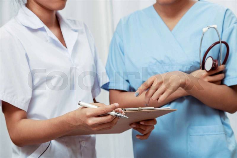 Nurses discussing pointing at a notepad about a patient’s record, stock photo