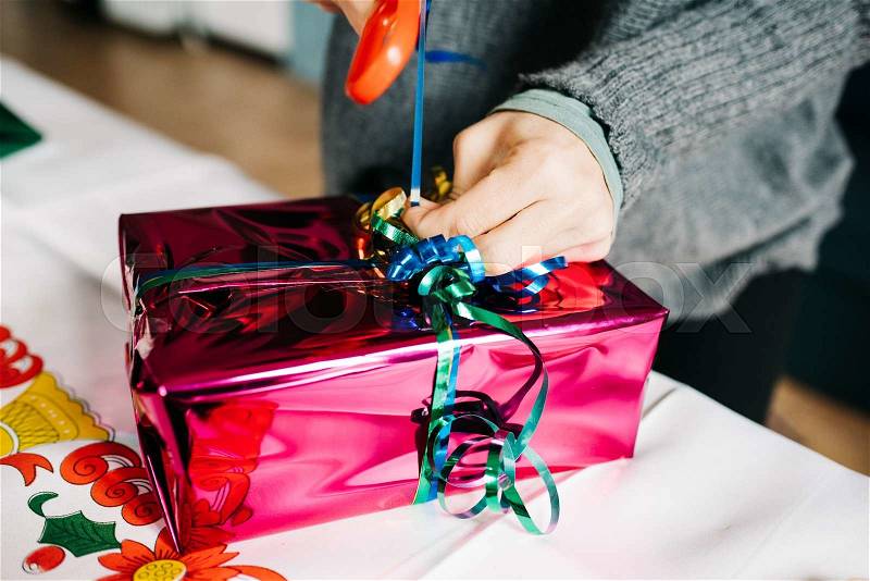 Close up on the hand of a young woman wrapping a christmas present, using scissor to make ribbon out of string - christmas, holiday, stock photo