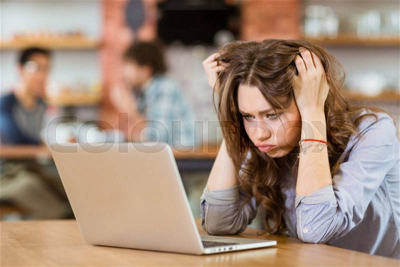 Exhausted stressed young woman with tousled hair sitting in cafe and using laptop, stock photo