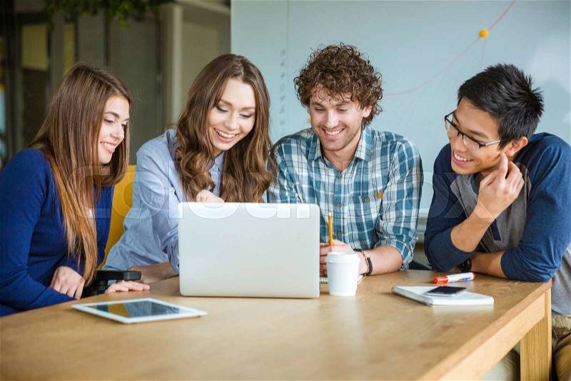 Group of positive cheerful students using laptop and doing homework together in classroom, stock photo