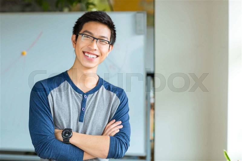 Portrait of a happy asian male student standing with arms folded in university, stock photo