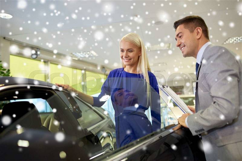 Auto business, car sale, consumerism and people concept - happy woman with car dealer in auto show or salon over snow effect, stock photo