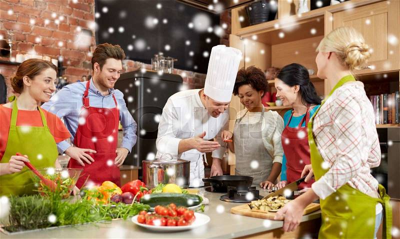 Cooking class, culinary, food and people concept - happy group of friends and male chef cook cooking in kitchen over snow effect, stock photo