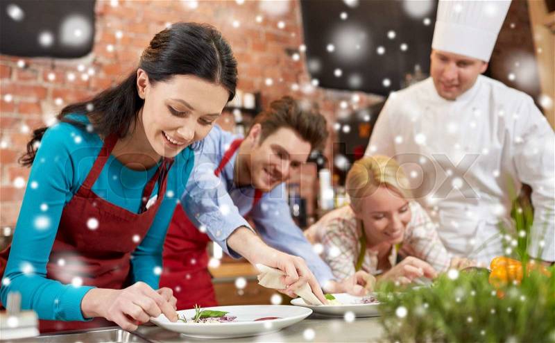 Cooking class, culinary, food and people concept - happy couple and male chef cook cooking and decorating plates in kitchen over snow effect, stock photo
