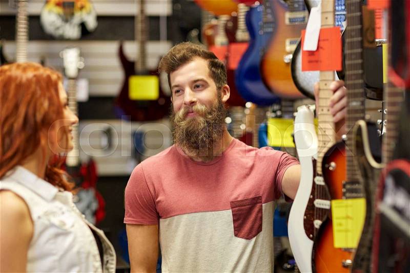 Music, sale, people, musical instruments and entertainment concept - happy couple of musicians choosing guitar at music store, stock photo